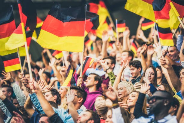 large group of people waving germany flags while standing on stadium bleachers.